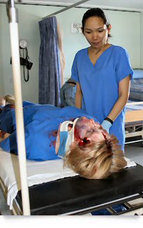 Woman with next brace in casualty make-up attended by nurse